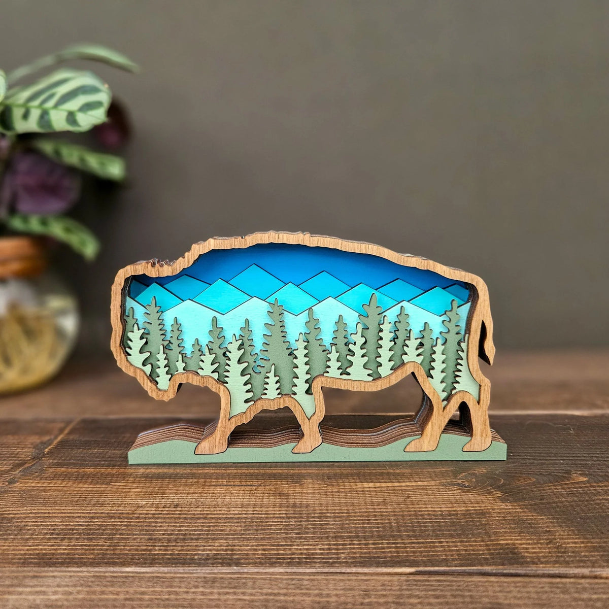 Wooden buffalo sculpture with a mountain and forest design on a wooden surface